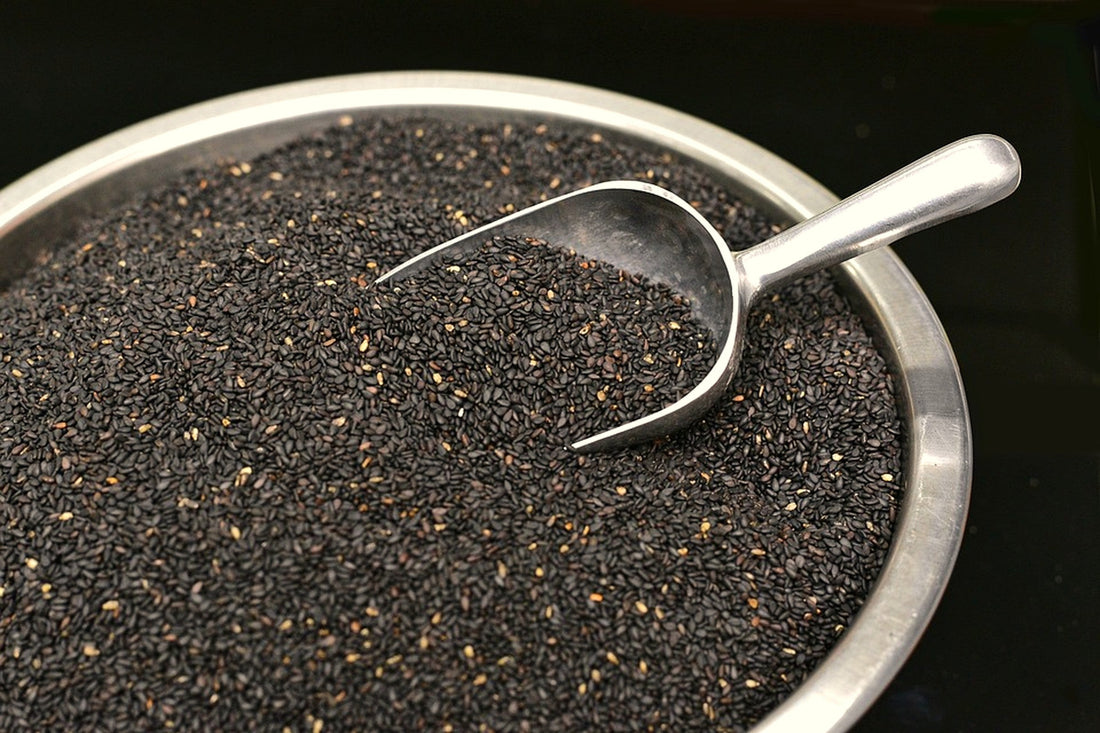 Stainless steel scoop filled with black sesame seeds in a metal bowl on dark background