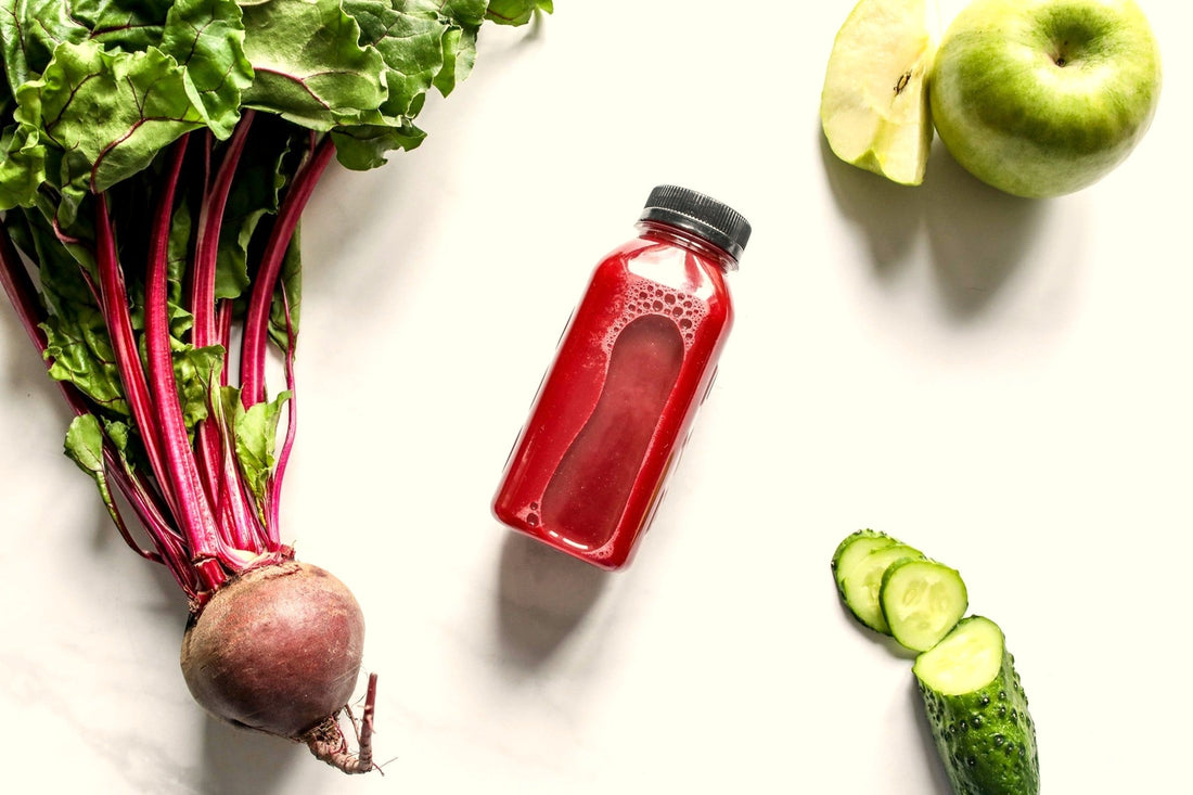Bottle of fresh beetroot juice with beet greens, apple, and cucumber on white background